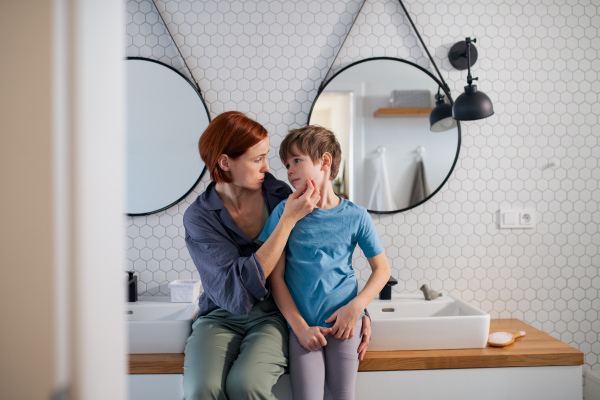 A mother hugging and talking with little son in bathroom at home.