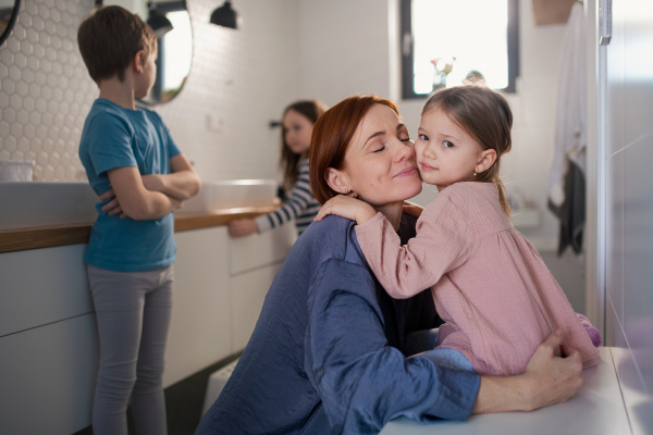 A mother of three little children hugging little daughter in bathroom at home.