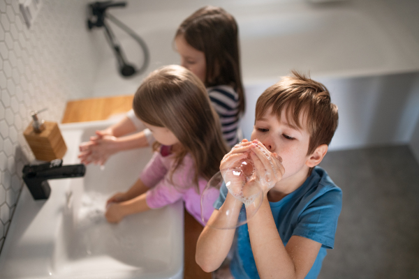 A high anbgle view of little children in bathroom, washing hands and doing bubbles from soap.