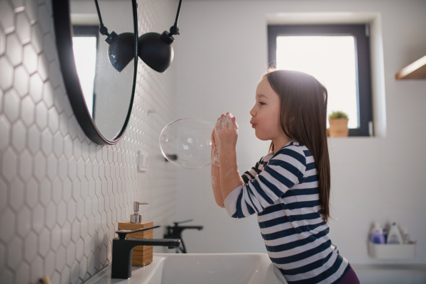 A little girl in bathroom, washing hands and doing bubbles from soap.