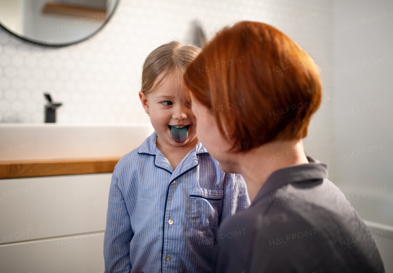 A little girl sticking showing her blue tongue to mother in bathroom at home.