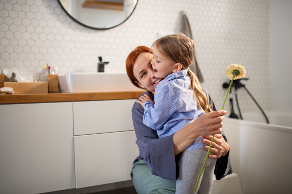 A little girl congratulates mother and gives her flower in bathroom at home.