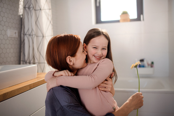 A little girl congratulates mother and gives her flower in bathroom at home.