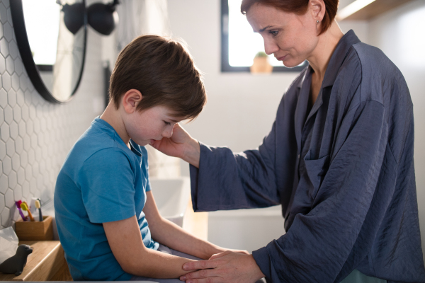 A mother consoling her little upset son in bathroom at home.