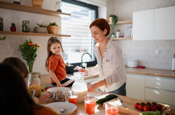 A mother of three little children preparing breakfast in kitchen at home.