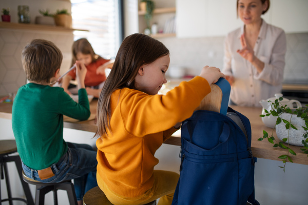 A little girl packing lunch box to backpack in kitchen at home.