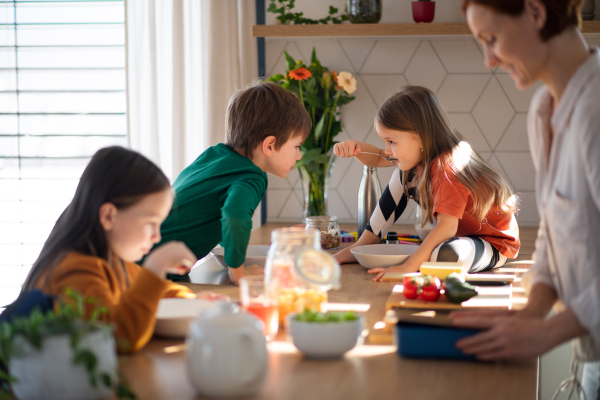 A mother of three little children preparing breakfast in kitchen at home.