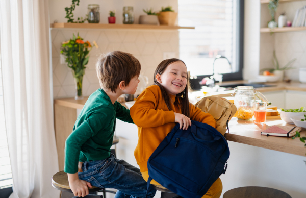 A little girl packing lunch box to backpack in kitchen at home.