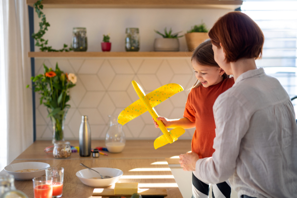 A rear view of mother with her little daughter in kitchen at home.