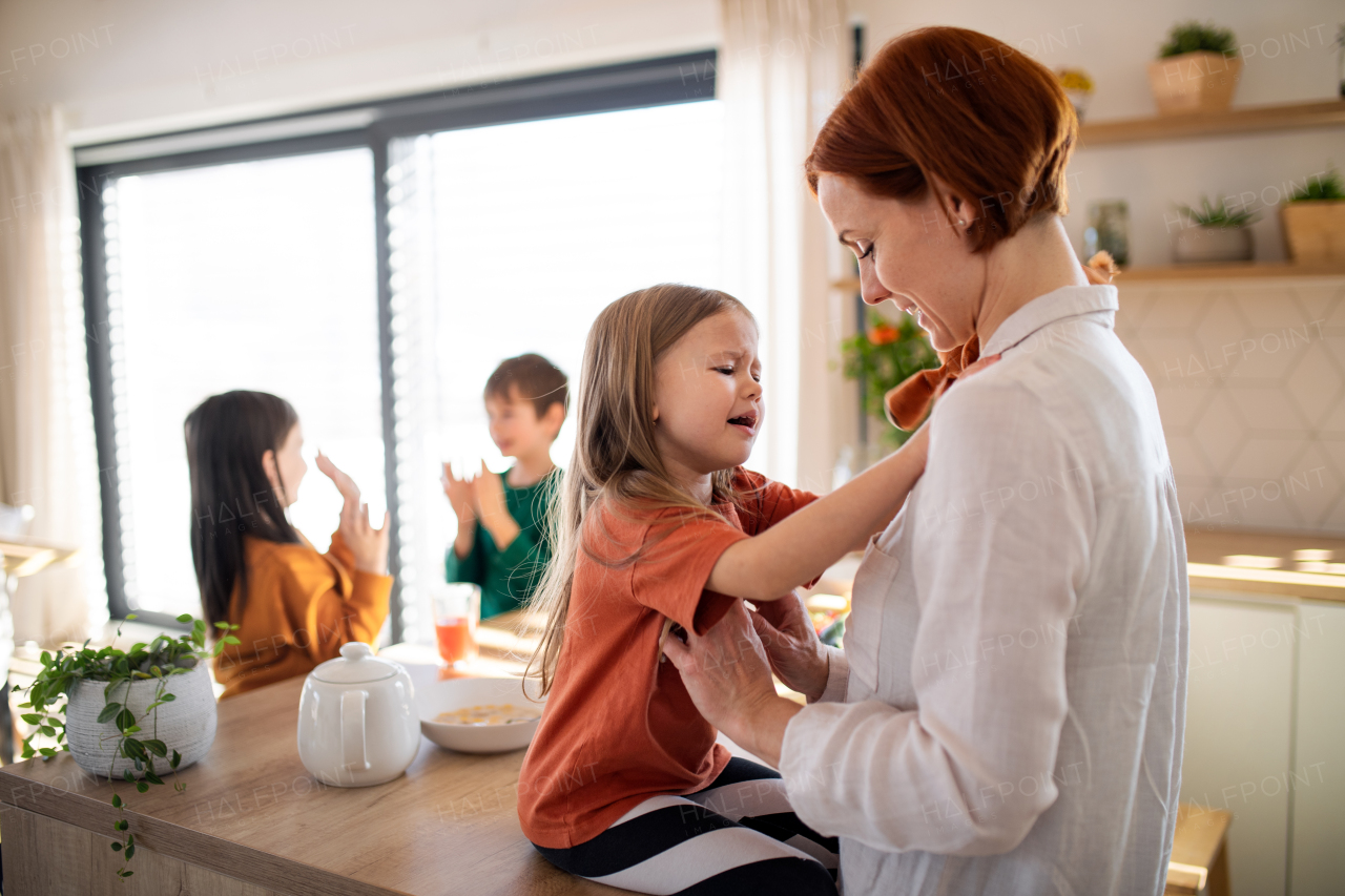 A mother embracing her little daughter in kitchen at home.