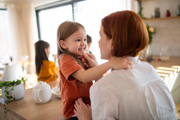 A rear view of mother embracing her little daughter in kitchen at home.