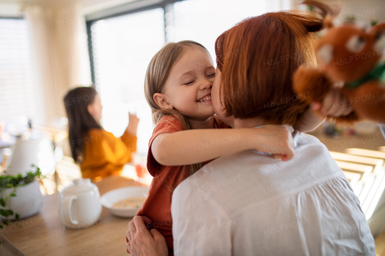 A rear view of mother hugging her little daughter in kitchen at home.