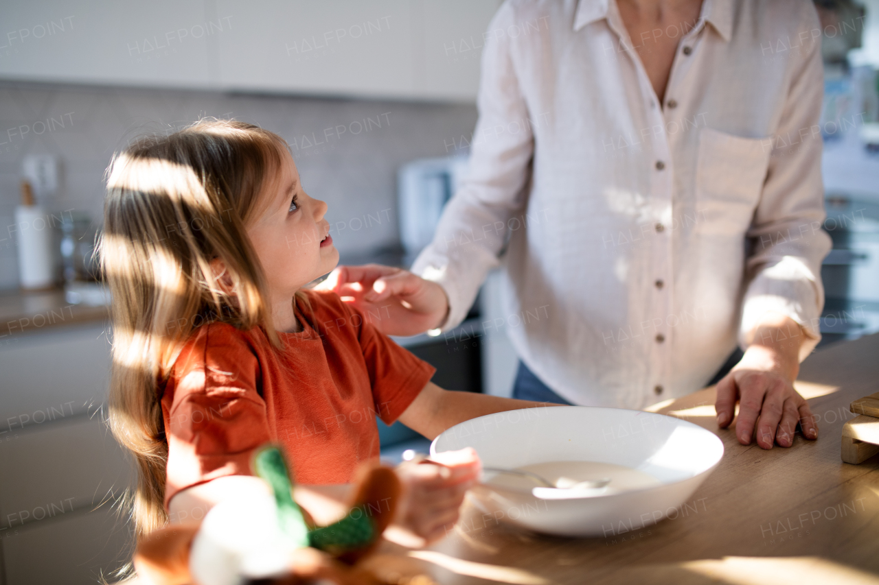 A little girl having breakfast with mother in kitchen.