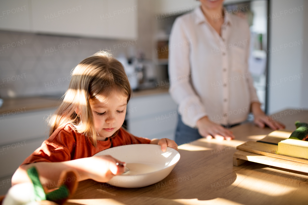 A little girl having breakfast with mother in kitchen.