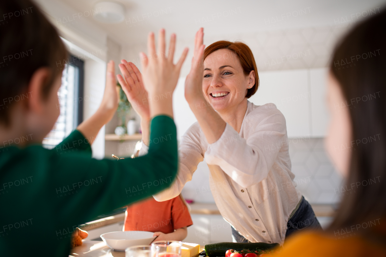 A happy mother high fiving with little son when having breakfast in kitchen at home.