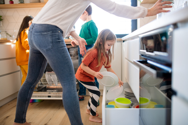 Three little chidlren helping a mother with dishes in kitchen at home.