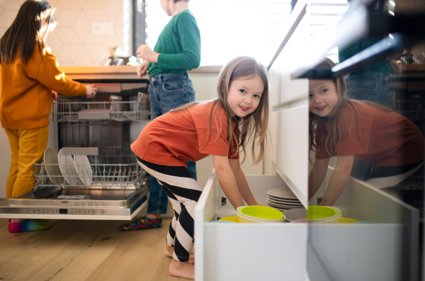 Three little chidlren helping with dishes in the kitchen at home.