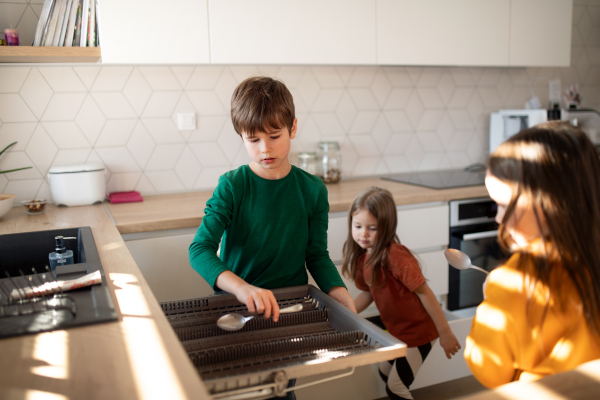 Three little chidlren helping with dishes in the kitchen at home.