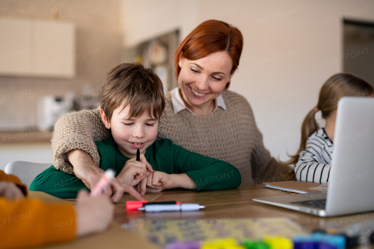 A mother of little children working on laptop when distance learning and doing artwork at home.