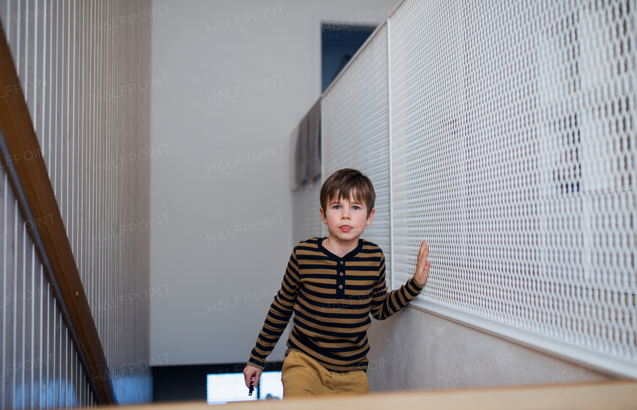 A little boy walking upstairs at home and looking at camera.