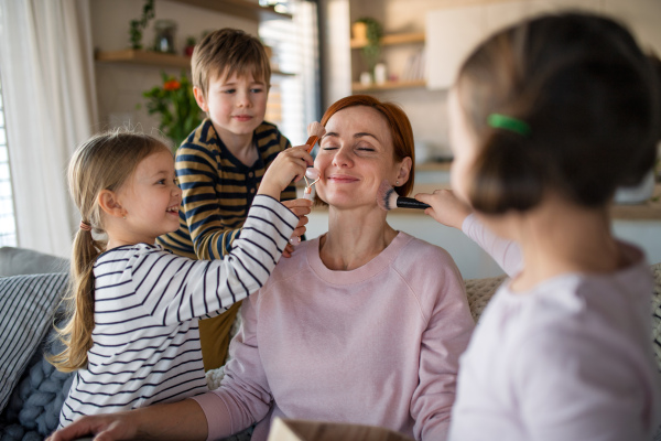 Three litttle children doing massage and apllying a make up to their mother at home.