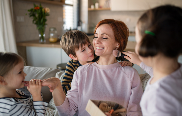 Three litttle children doing massage and apllying a make up to their mother at home.