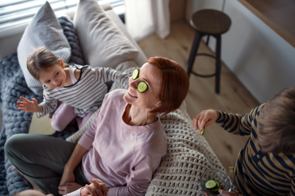 A high angle view of little children putting cucumber on their mother's face at home.