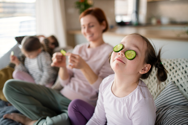 Little chidlren with mother putting a cucumber on faces at home.