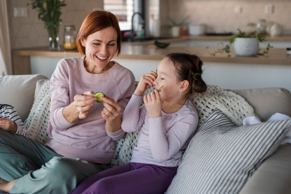 Little children with mother putting a cucumber on faces at home.