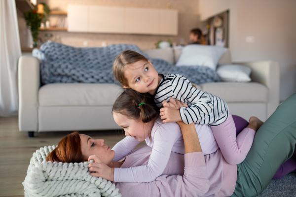 Little children lying on her mother and having fun in a living room at home.