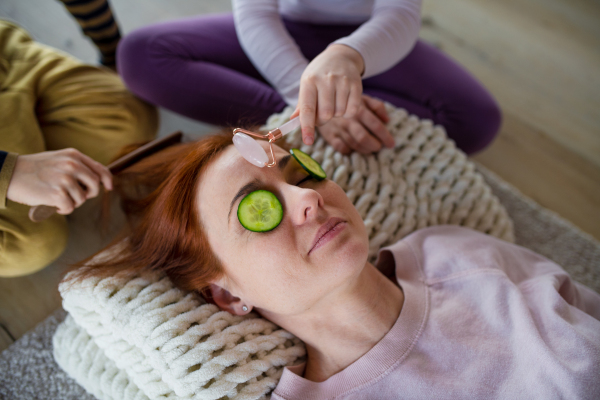 Little chidlren putting cucumber on their mother's face and doing a face massage to her at home.