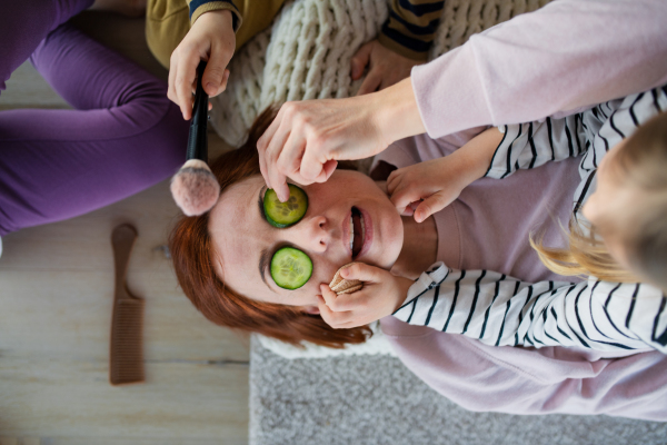 Little chidlren putting cucumber on their mother's face and applying a make up to her at home.