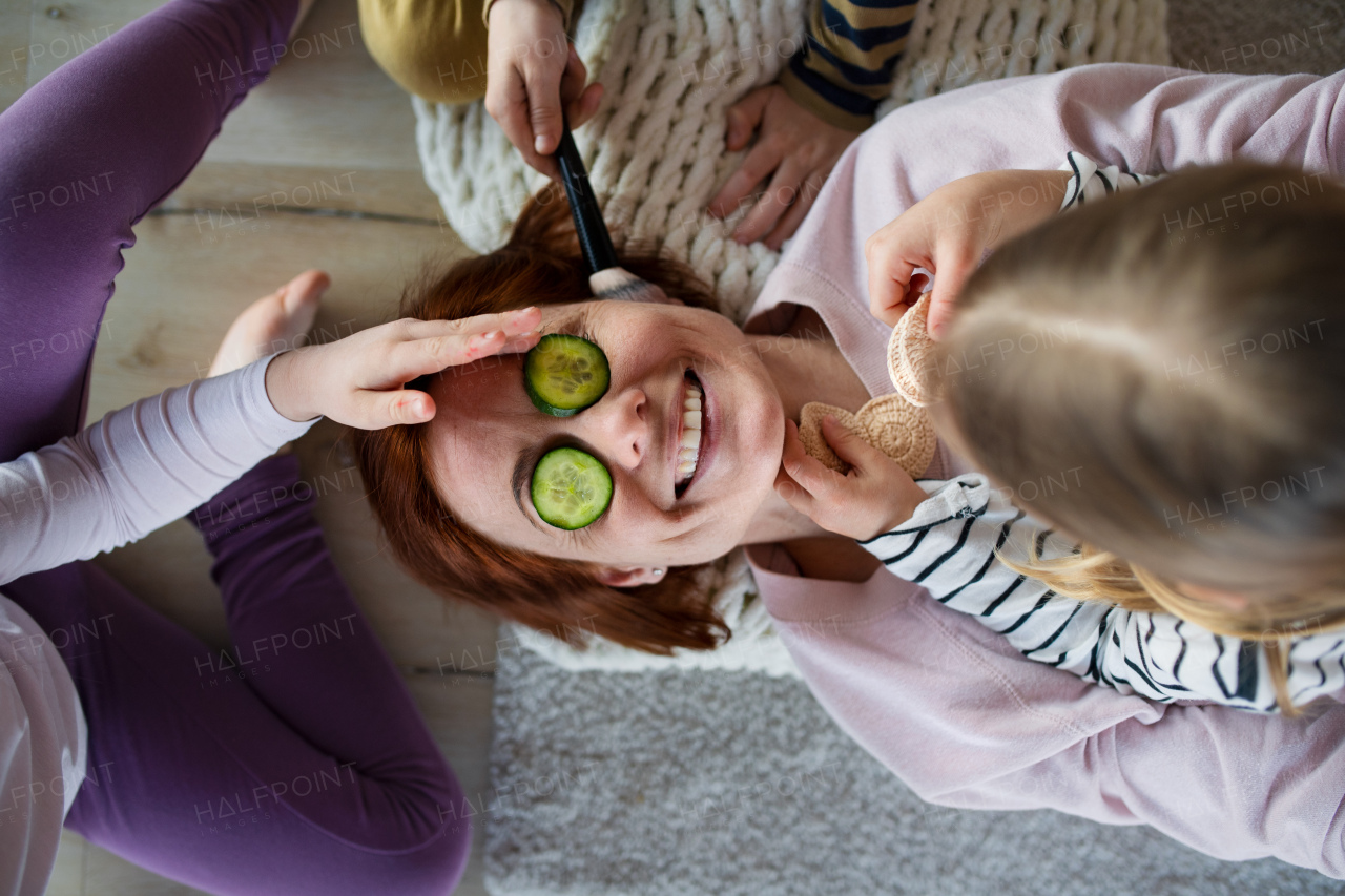 Little chidlren putting cucumber on their mother's face and applying a make up to her at home.