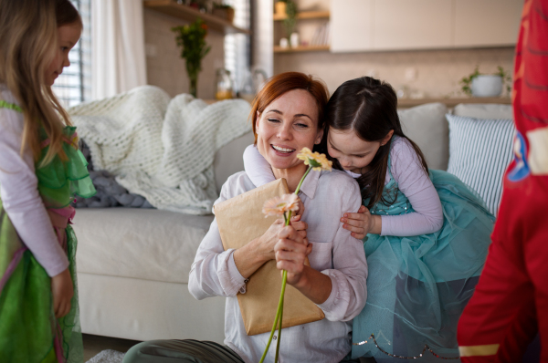 A mother of three little children in costumes getting present from them at home.