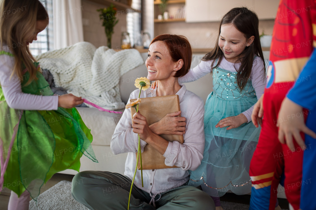 A mother of three little children in costumes getting present and flower from them at home.