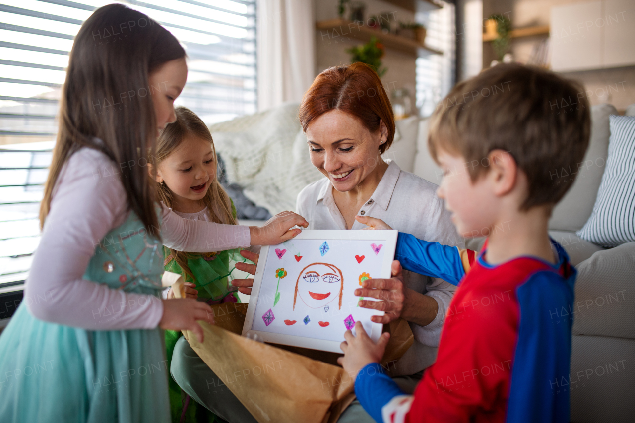 A mother of little children in costumes getting present from them at home.