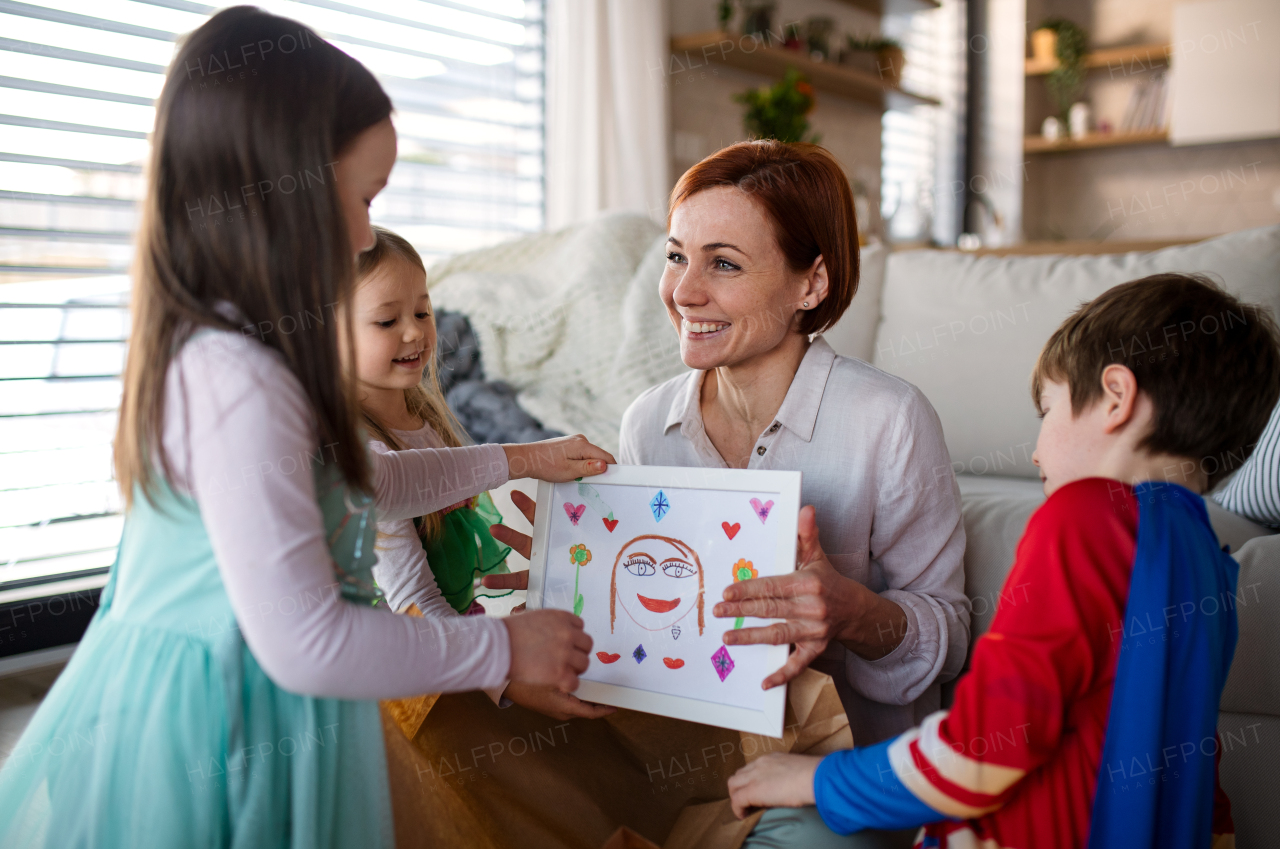 A mother of little children in costumes getting present from them at home.