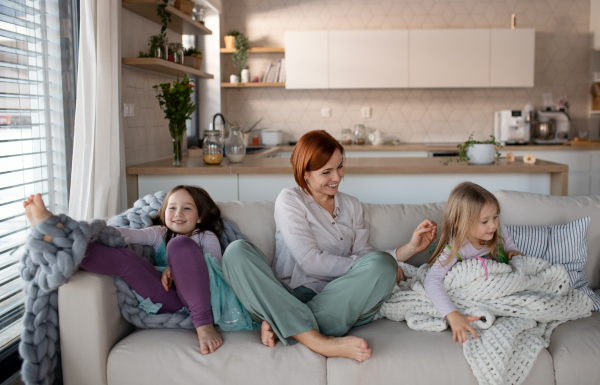 A mother with two little daugter sitting on sofa and resting at home.