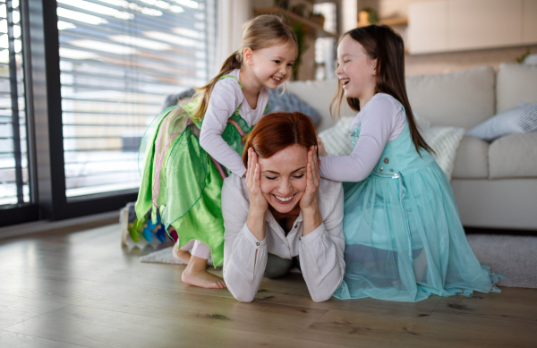 A happy mother having fun with little daughters in princess costumes at home.