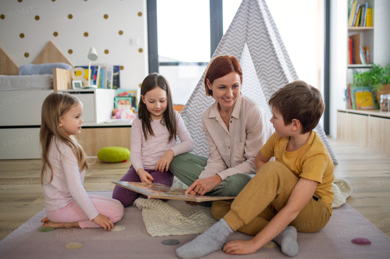 A cheerful mother of three little children reading them book at home.