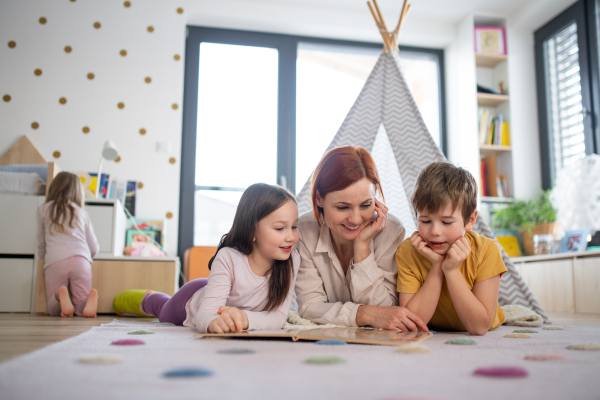 A cheerful mother of three little children reading them book at home.