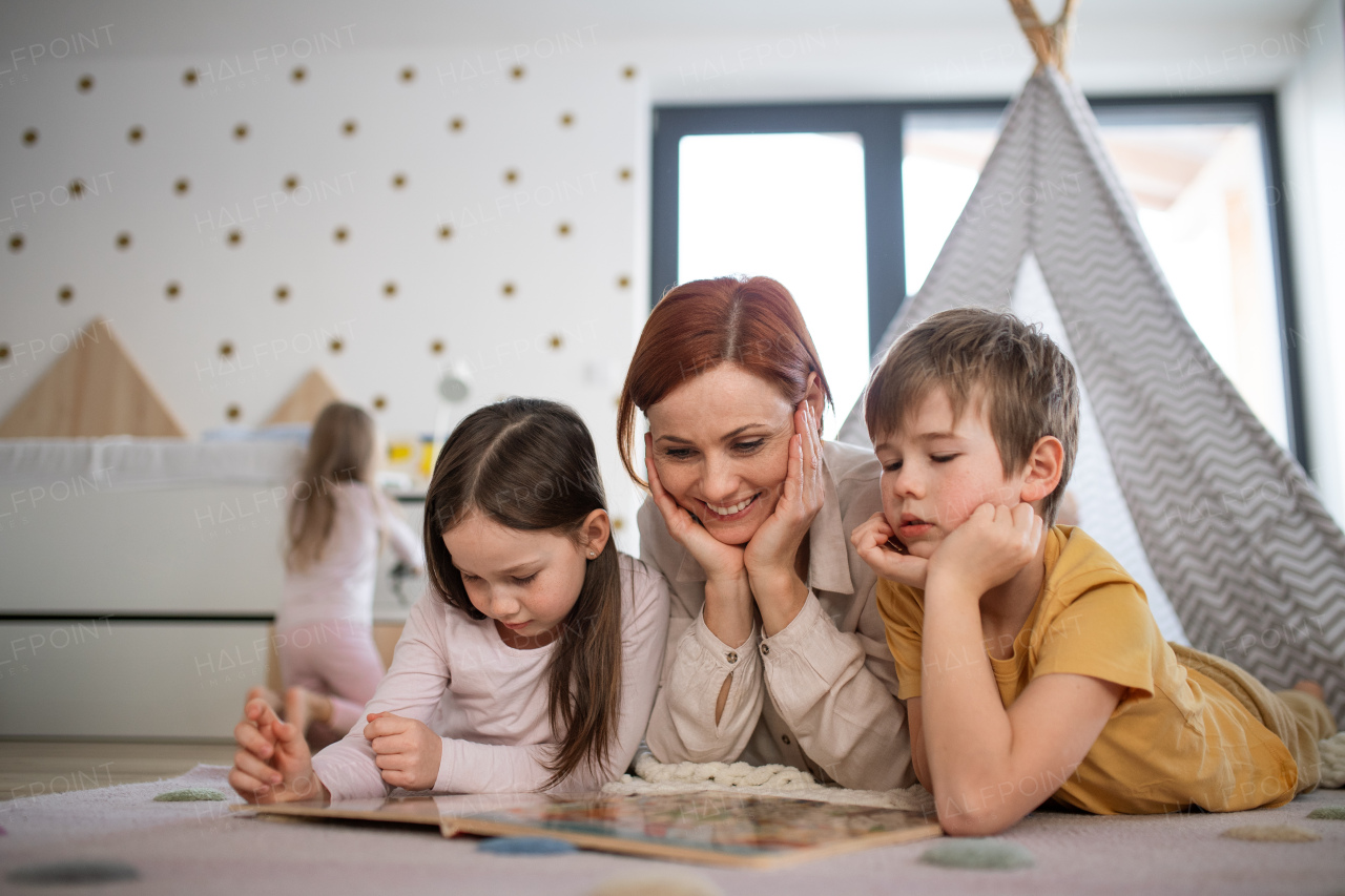 A mother with little children lying on floor and reading book at home.