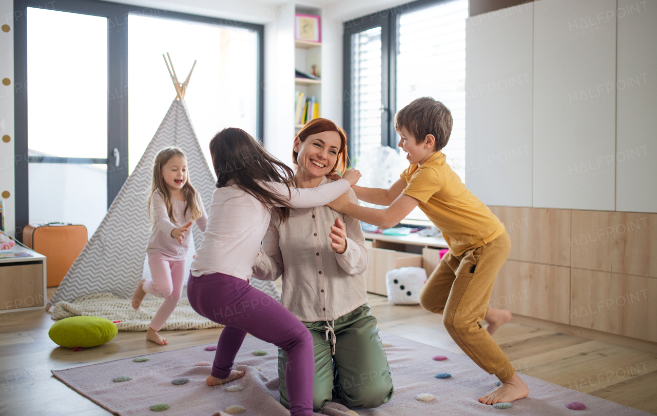 A cheerful mother of three little children receiving hugs from them at home.