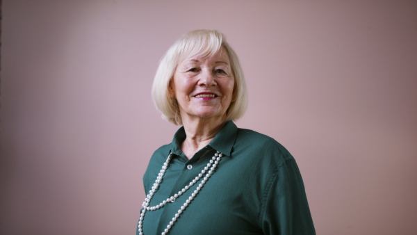 A smiling elegant elderly woman on pink color background, studio shooting