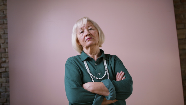 A sad elegant elderly woman on pink color background, studio portrait