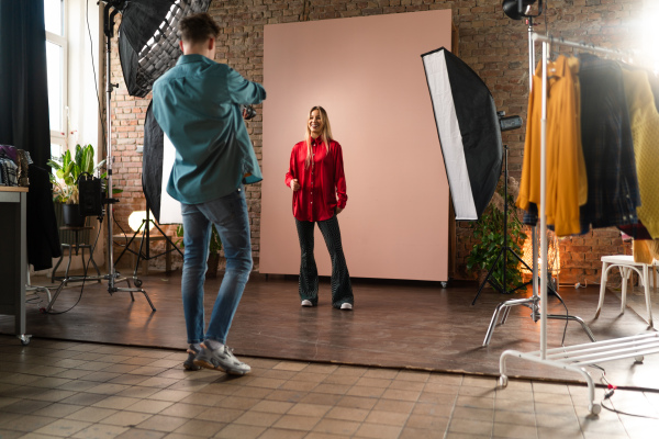 A young photographer taking picures of model, backstage of photoshooting in studio.