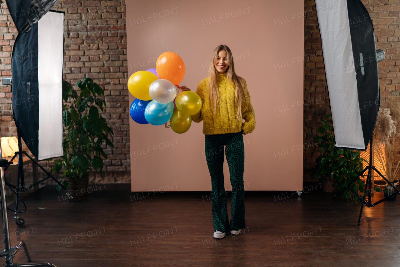 A studio portrait of a happy young blonde woman with balloon over pink background.