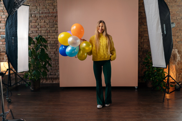 A studio portrait of a happy young blonde woman with balloon over pink background.