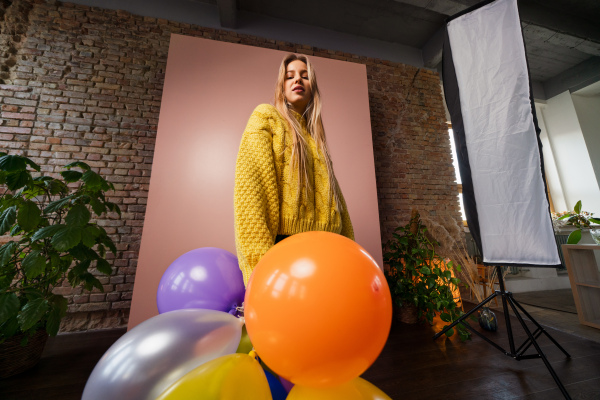 A studio portrait of a happy young blonde woman with balloon over pink background. Low angle view.