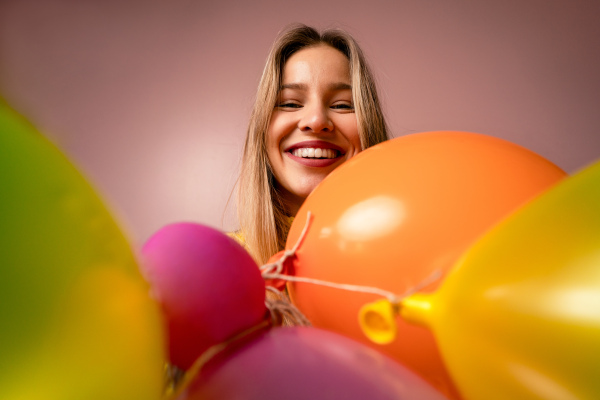 A studio portrait of a happy young blonde woman with balloons over pink background.